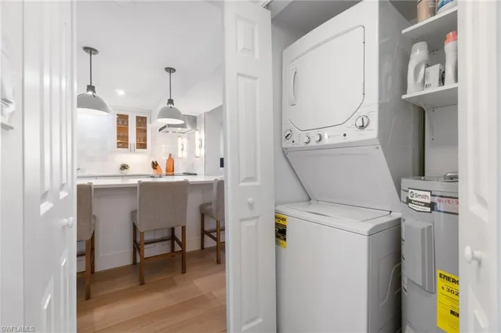 Laundry area with water heater, light wood-style flooring, and stacked washer and dryer