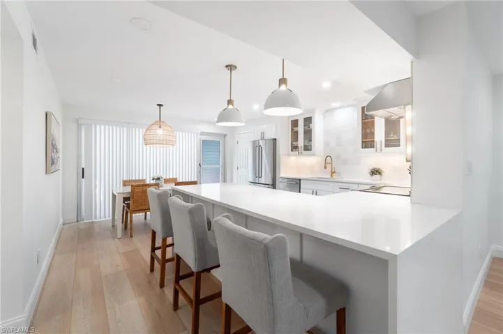 Kitchen with glass insert cabinets, a kitchen breakfast bar, a peninsula, pendant lighting, and light wood-type flooring