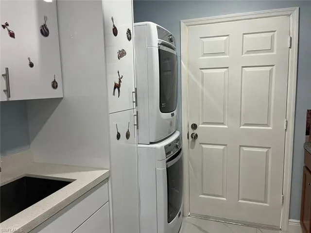 Clothes washing area featuring stacked washer / drying machine, cabinets, and sink
