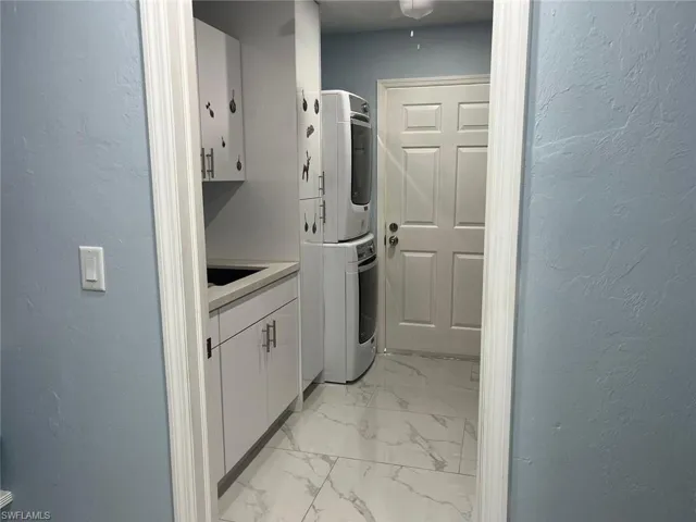 Laundry room featuring stacked washer / drying machine and cabinets