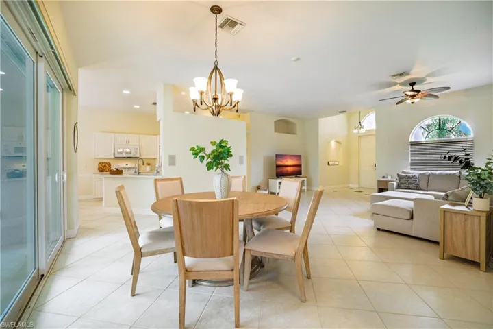 Kitchen featuring white appliances, a peninsula, light tile patterned floors, suspended lighting, and white cabinets