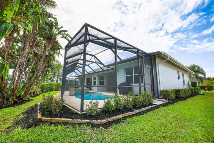 Back of house featuring a sunroom, a patio area, an outdoor pool, a lawn, and stucco siding