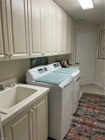Clothes washing area with cabinets, light tile patterned floors, independent washer and dryer, and sink