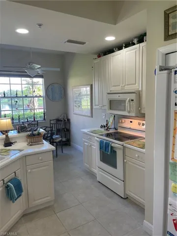 Kitchen with white cabinets, light tile patterned floors, refrigerator, ceiling fan, and range