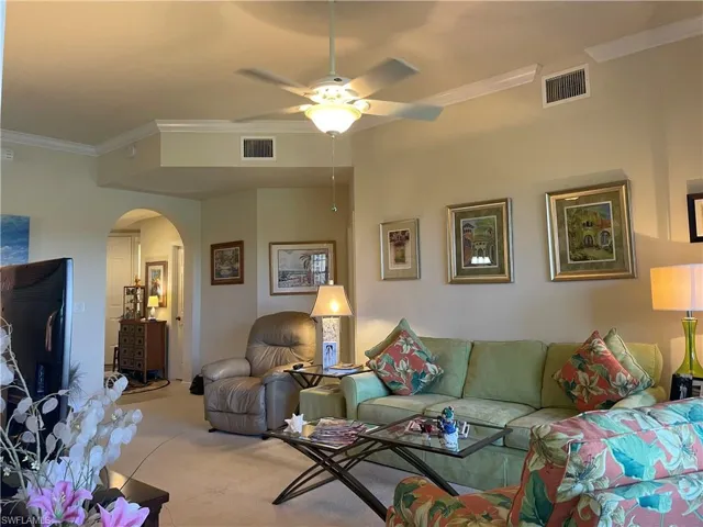 Carpeted living room featuring ceiling fan and crown molding