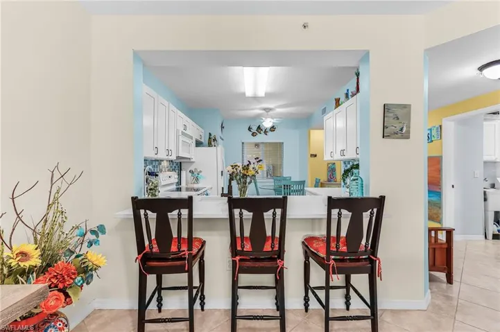 Kitchen with a breakfast bar, light countertops, white appliances, white cabinets, and light tile patterned floors