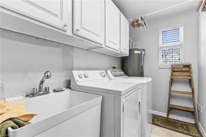 Laundry area featuring cabinet space, separate washer and dryer, electric water heater, and light tile patterned floors