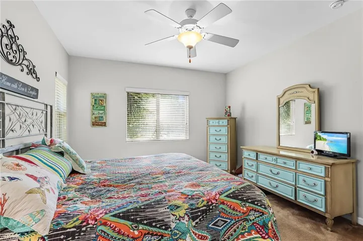 Bedroom with dark carpet, multiple windows, and ceiling fan