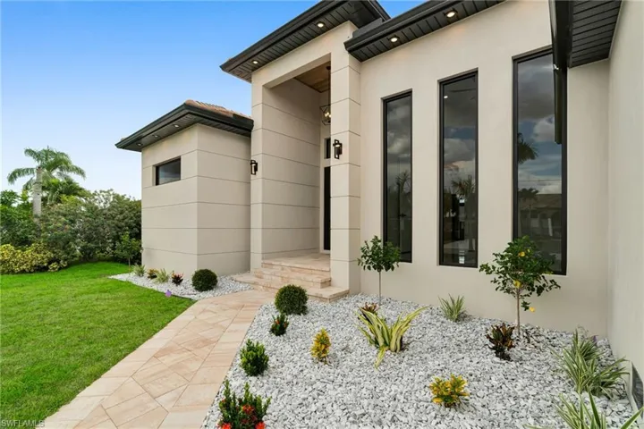 View of exterior entry with stucco siding and a lawn