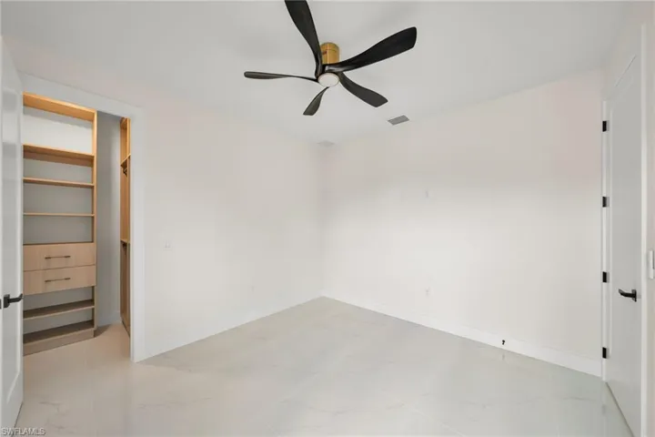 Unfurnished bedroom featuring light marble finish flooring, ceiling fan, and a walk in closet