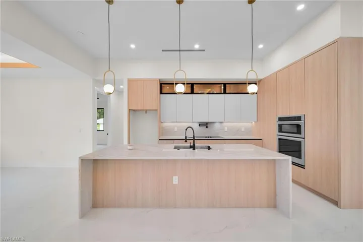 Kitchen featuring modern cabinets, light brown cabinets, tasteful backsplash, double oven, and light stone counters