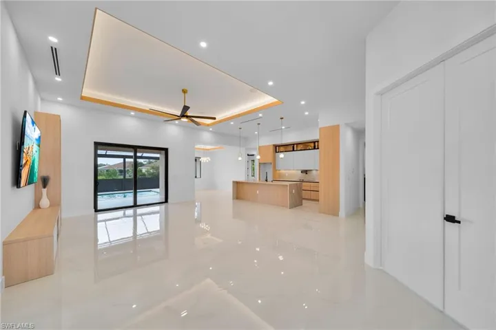 Unfurnished living room with a tray ceiling, ceiling fan, light marble finish flooring, and recessed lighting