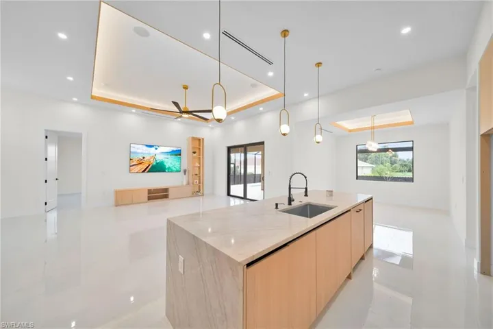 Kitchen with modern cabinets, a raised ceiling, light brown cabinetry, open floor plan, and healthy amount of natural light