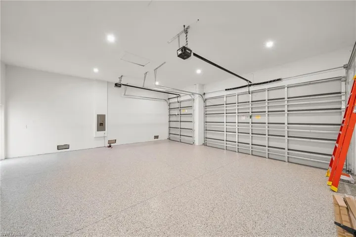 Garage with a garage door opener, electric panel, and recessed lighting