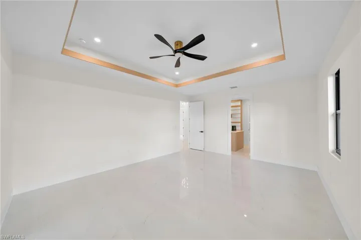 Spare room with a tray ceiling, light marble finish flooring, a ceiling fan, and recessed lighting