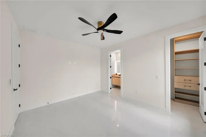 Unfurnished bedroom featuring a walk in closet, connected bathroom, ceiling fan, and light marble finish floors