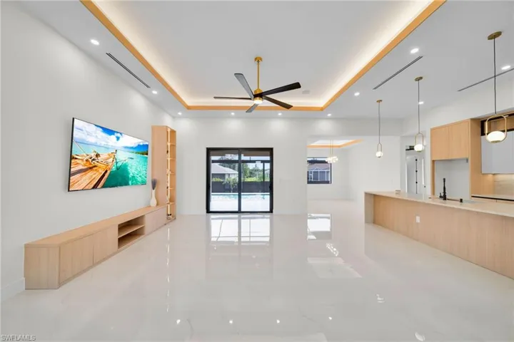 Unfurnished living room with a tray ceiling, light marble finish floors, a ceiling fan, and recessed lighting