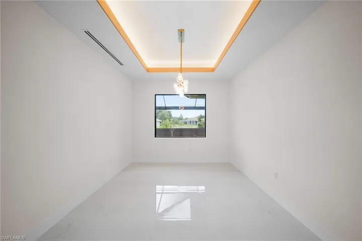 Spare room with light marble finish floors, a raised ceiling, and a chandelier