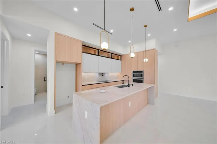 Kitchen with modern cabinets, light brown cabinetry, tasteful backsplash, stainless steel double oven, and a center island with sink