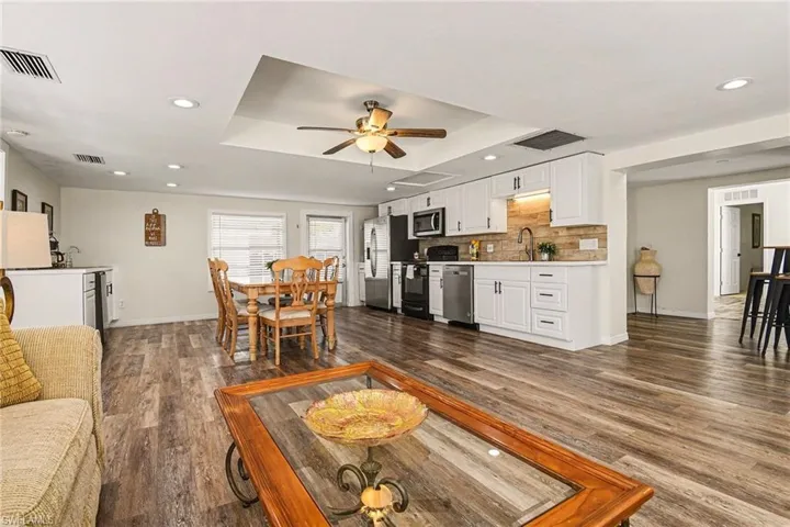 Living area with a raised ceiling, wood-style flooring, a ceiling fan, and recessed lighting