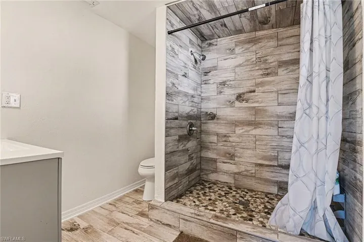 Full bathroom featuring vanity, tiled shower, and wood finish floors