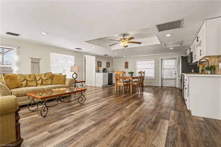 Living area with wood finished floors, healthy amount of natural light, a raised ceiling, ceiling fan, and recessed lighting