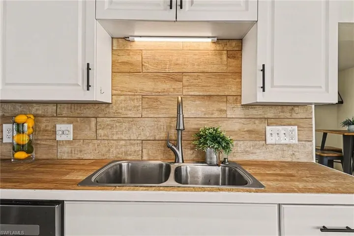 Kitchen featuring white cabinets, backsplash, butcher block countertops, and dishwasher