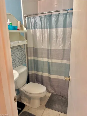 Full bath featuring toilet, a shower with curtain, and tile patterned floors