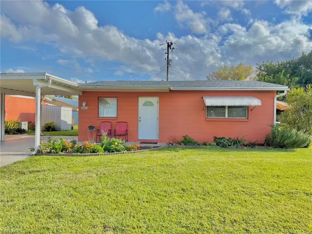View of front of property with a front yard, concrete driveway, and an attached carport