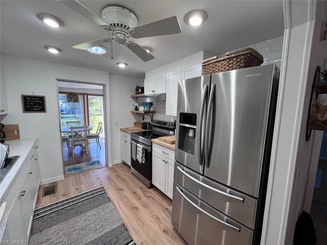 Kitchen with backsplash, stainless steel appliances, ceiling fan, white cabinets, and light hardwood / wood-style floors
