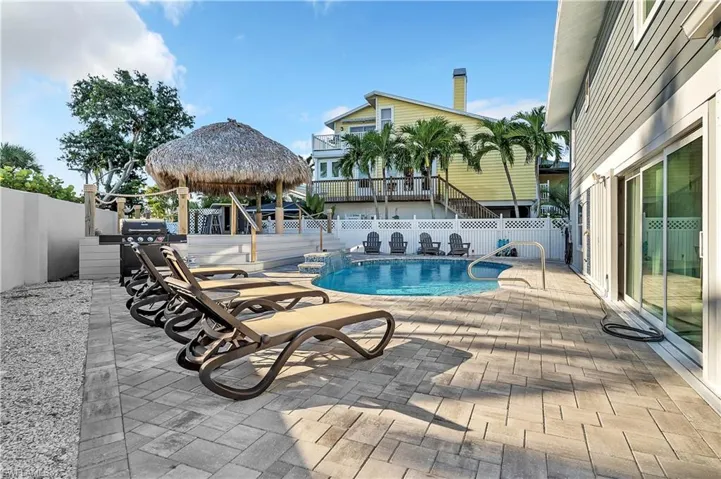 Backyard featuring a paver patio, in-ground swimming pool, elevated tiki-style hut, and perimeter privacy fencing