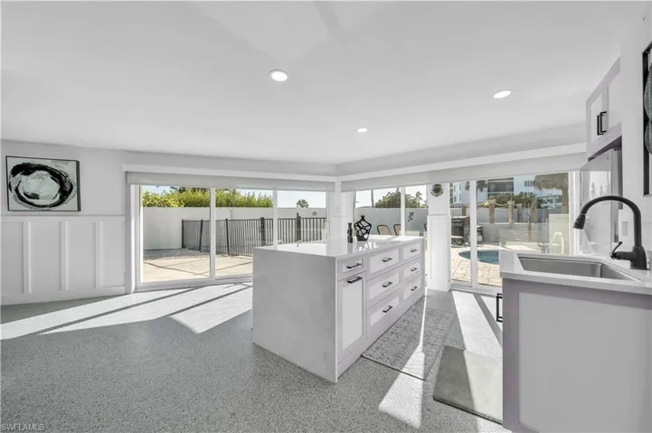 Kitchen featuring a central island with a solid surface countertop, matte black faucet hardware, recessed ceiling lighting, wainscoting detail, and dual sets of floor-to-ceiling sliding glass doors
