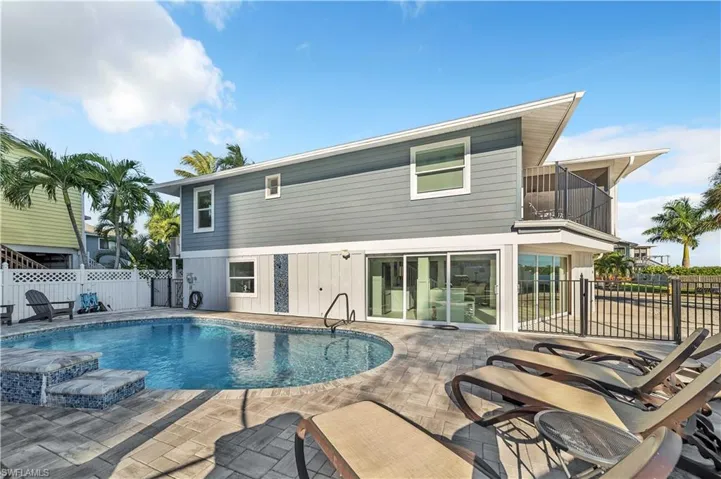 Exterior featuring horizontal lap and board-and-batten siding, in-ground swimming pool with mosaic tile steps, expansive paver patio, second-story balcony with metal railing, and multi-panel sliding glass doors