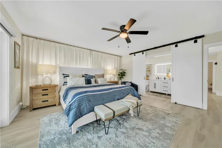 Spacious room featuring wood-finish flooring, dual sliding barn doors, a central ceiling fan with integrated lighting, and a white vanity with an illuminated wall mirror