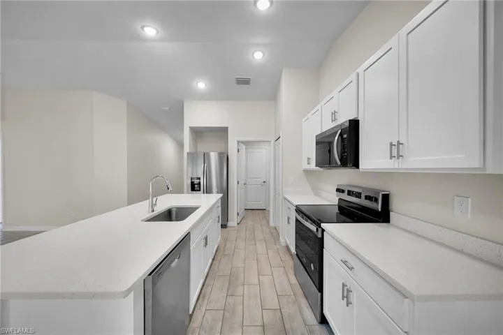Modern kitchen with white cabinetry, stainless steel appliances, wood-finish flooring, recessed lighting, and expansive countertops