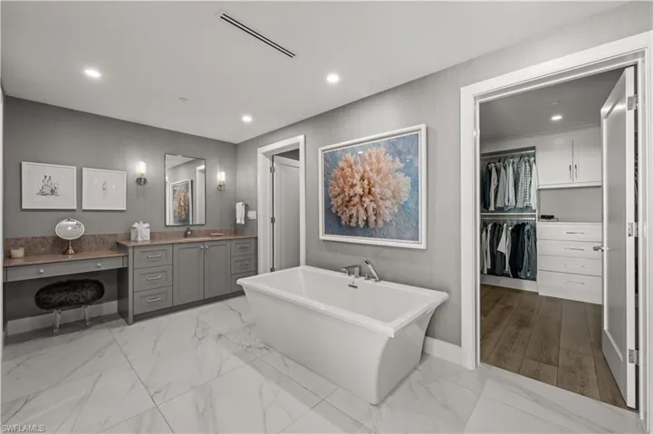 Bathroom featuring vanity, a walk in closet, a freestanding bath, light marble finish floors, and recessed lighting