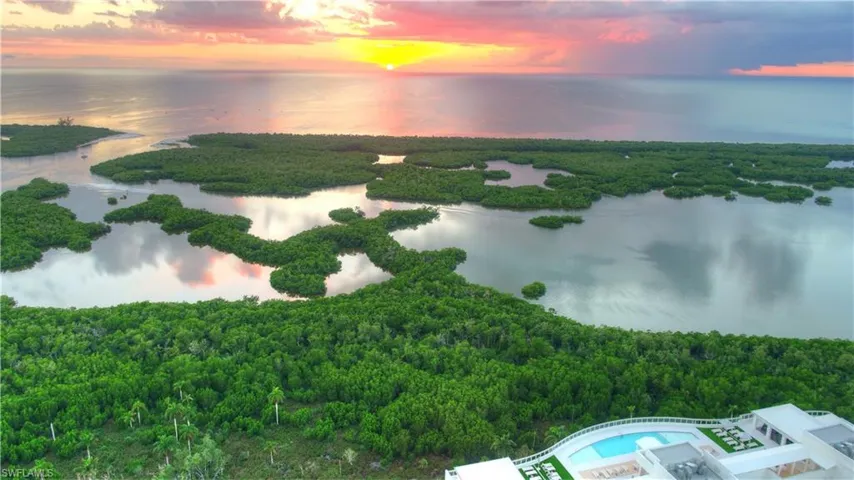 Aerial view at dusk of a water view, a view of trees, and view of pool area