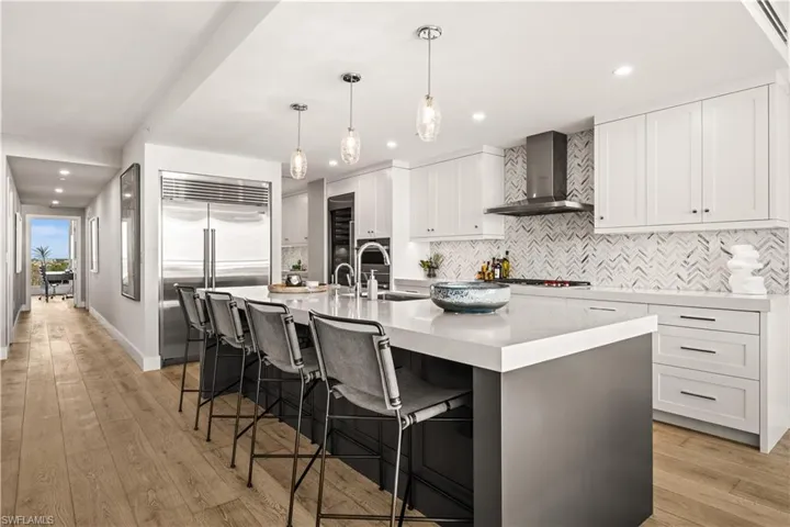 Kitchen with a breakfast bar area, a spacious island, light wood-style floors, stainless steel appliances, and pendant lighting