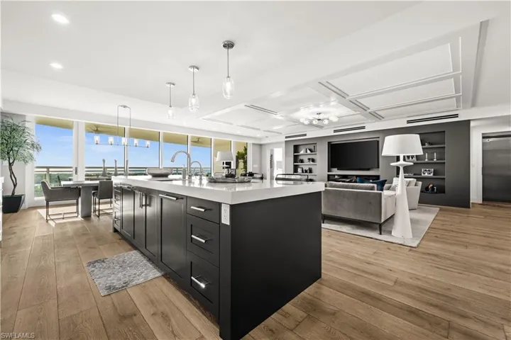 Kitchen with dark cabinetry, light wood-style flooring, a center island with sink, and decorative light fixtures