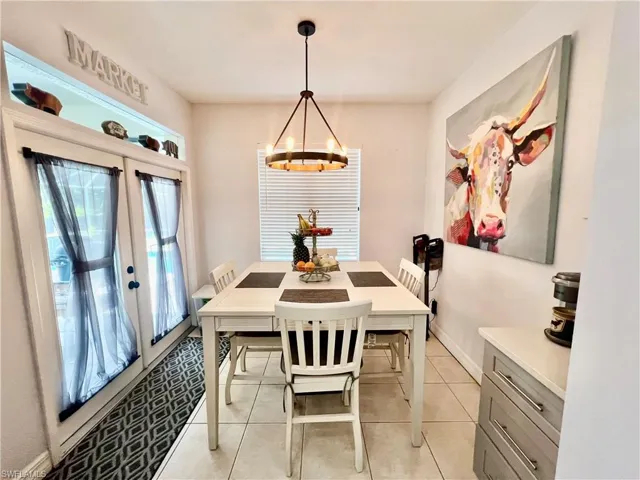Dining space with light tile patterned floors, french doors, baseboards, and a notable chandelier