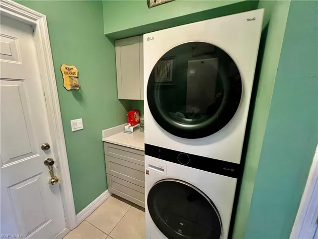 Laundry room with cabinet space, light tile patterned floors, baseboards, and stacked washer / drying machine