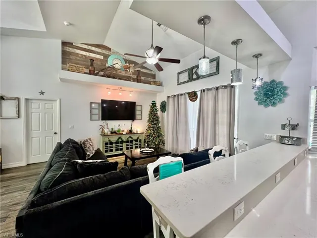 Living room featuring a ceiling fan, QUARTZ BREAKFAST BAR, high vaulted ceiling, and wood finished floors