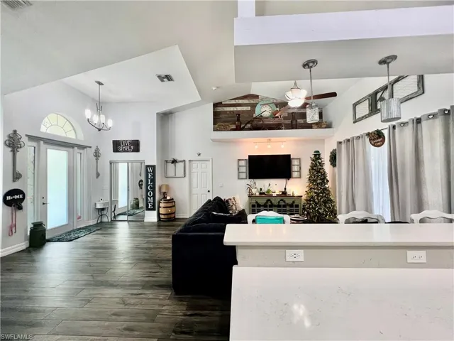 Living area featuring high vaulted ceiling, visible vents, baseboards, wood-style floors.