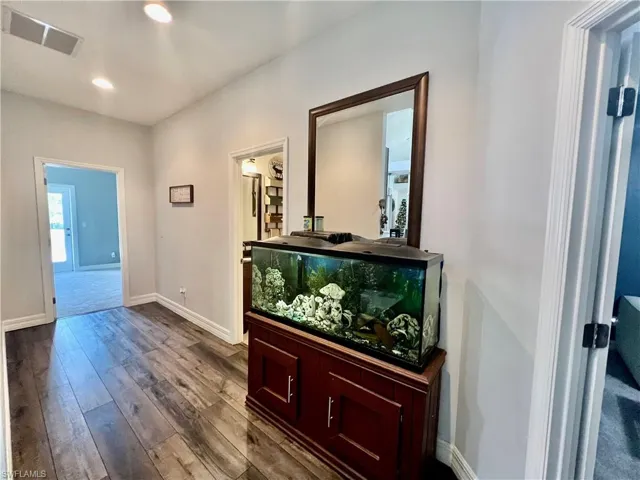 Wide guest hallway with recessed lighting, visible vents,  wood finished floors, and baseboards