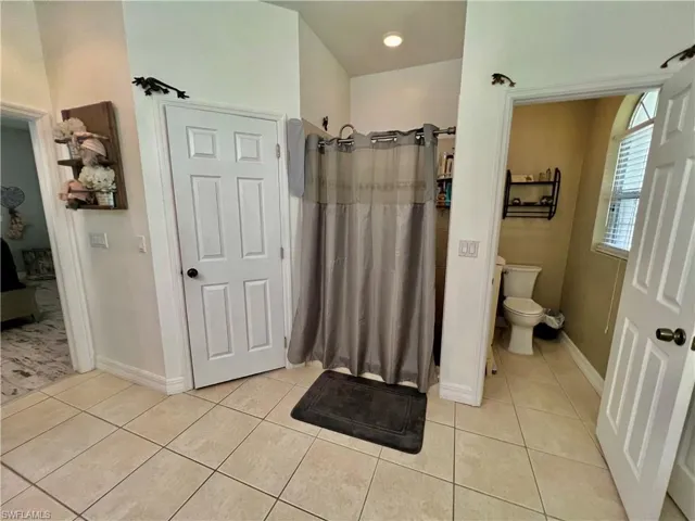 Primary bathroom with toilet, curtained shower, tile patterned flooring, and baseboards