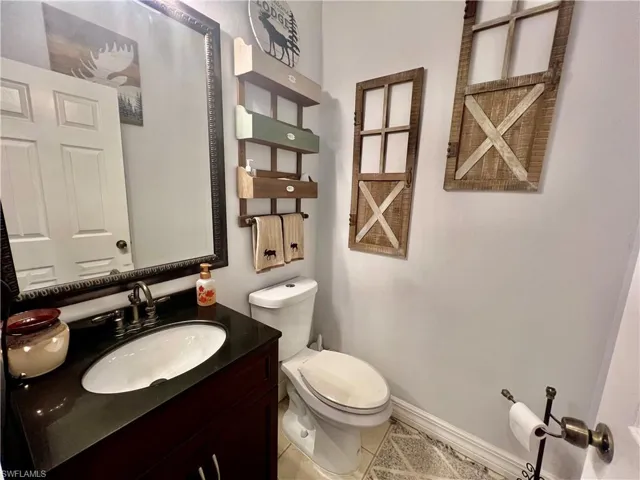 Half bathroom off of the main living area with tile patterned flooring, vanity, toilet, and baseboards