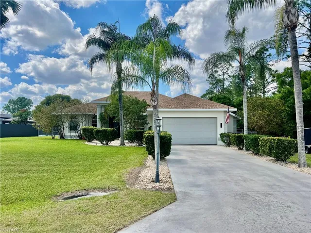 Ranch-style home with long concrete driveway lined with palm trees.