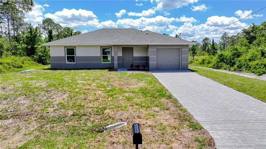 Ranch-style home with stucco siding, decorative driveway, a front yard, an attached garage, and a shingled roof