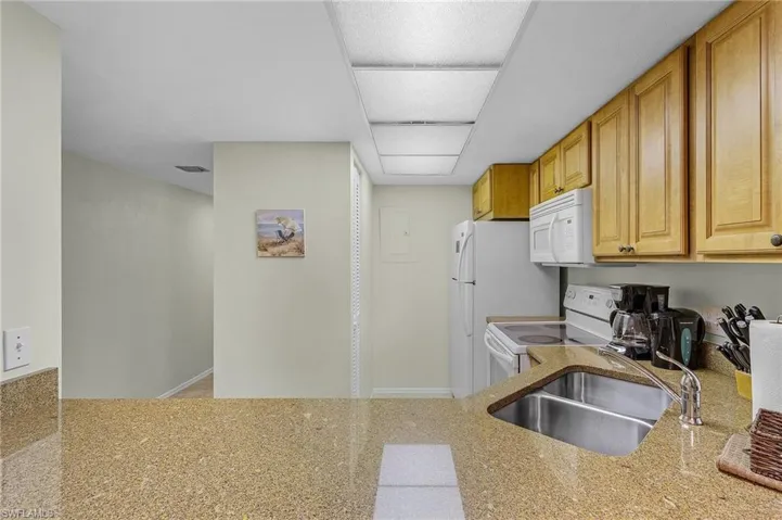 Kitchen with kitchen peninsula, white appliances, light stone counters, and sink