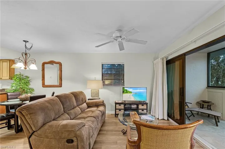 Living room with ceiling fan with notable chandelier and light hardwood / wood-style floors